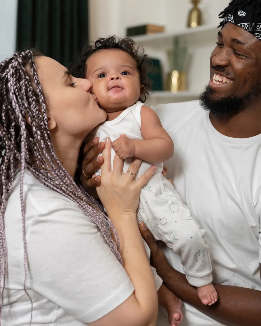 Parents smiling and kissing their baby at home